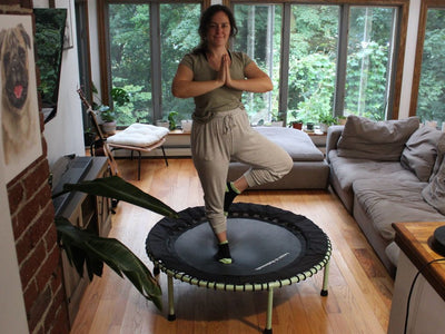 Person balancing on trampoline in living room, surrounded by plants.