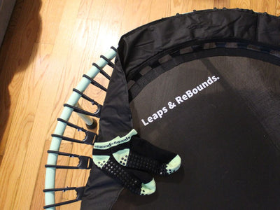 Mini trampoline with grip socks on it, wooden floor background.