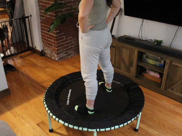 Person standing on indoor trampoline in living room, hands on hips.