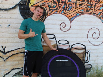 Person standing by a trampoline, colorful mural in background.