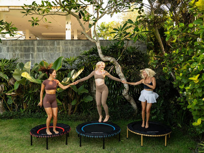 Three people jumping on trampolines outdoors, surrounded by greenery.