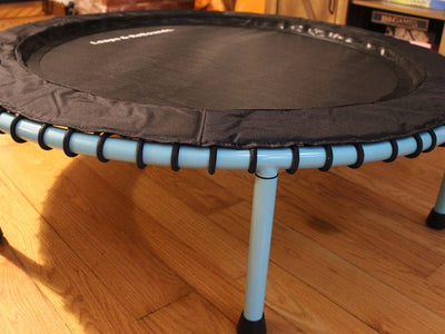 Small indoor trampoline with blue legs on wooden floor.