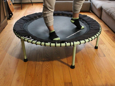 Person standing on mini trampoline in living room, wearing socks.