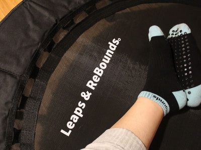 Person wearing grip socks sitting on a mini trampoline, indoors.