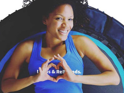 Person lying on trampoline, smiling, making heart shape with hands.