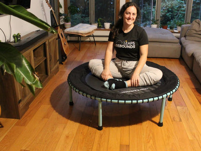 Person sitting cross-legged on mini trampoline in cozy living room.